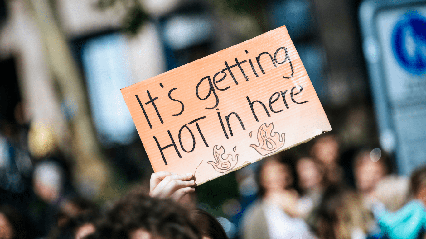 Person hält ein Schild hoch mit der Aufschrift: "It's getting Hot in here"